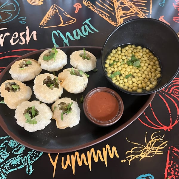 Pani Puri on a black plate with a bowl of boondi and a small bowl of red chutney.