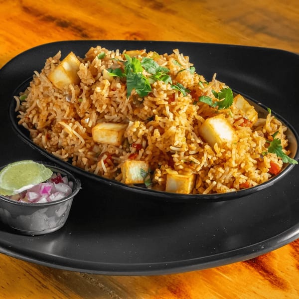 Paneer Biryani with cilantro, served on a black plate with a side of pickled onions and lime.